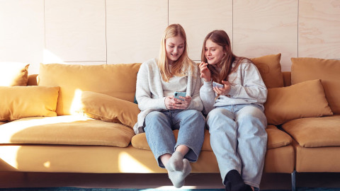 Nuoret katsovat älypuhelinta hymyillen sohvalla