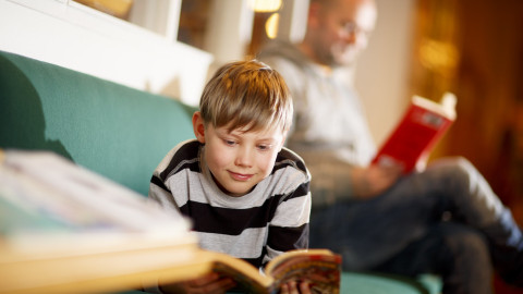 Lapsi ja aikuinen ovat sohvalla lukemassa kumpikin omaa kirjaansa. Kuva Hanna-Kaisa Hämäläinen