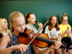 Tyttö soittaa viulua ja muut laulavat taustalla. Kuva Hanna-Kaisa Hämäläinen