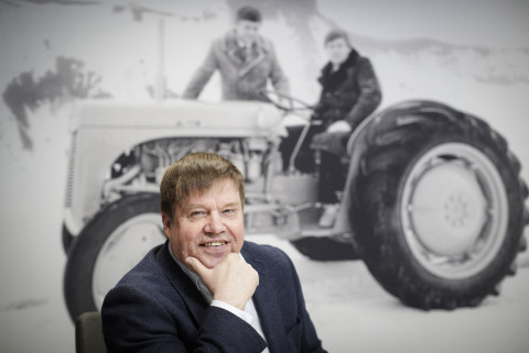 Kuvan etuosassa mies ja hänen takanaan vanha kuva, jossa traktori ja kaksi miestä. Kuva Petteri Kivimäki